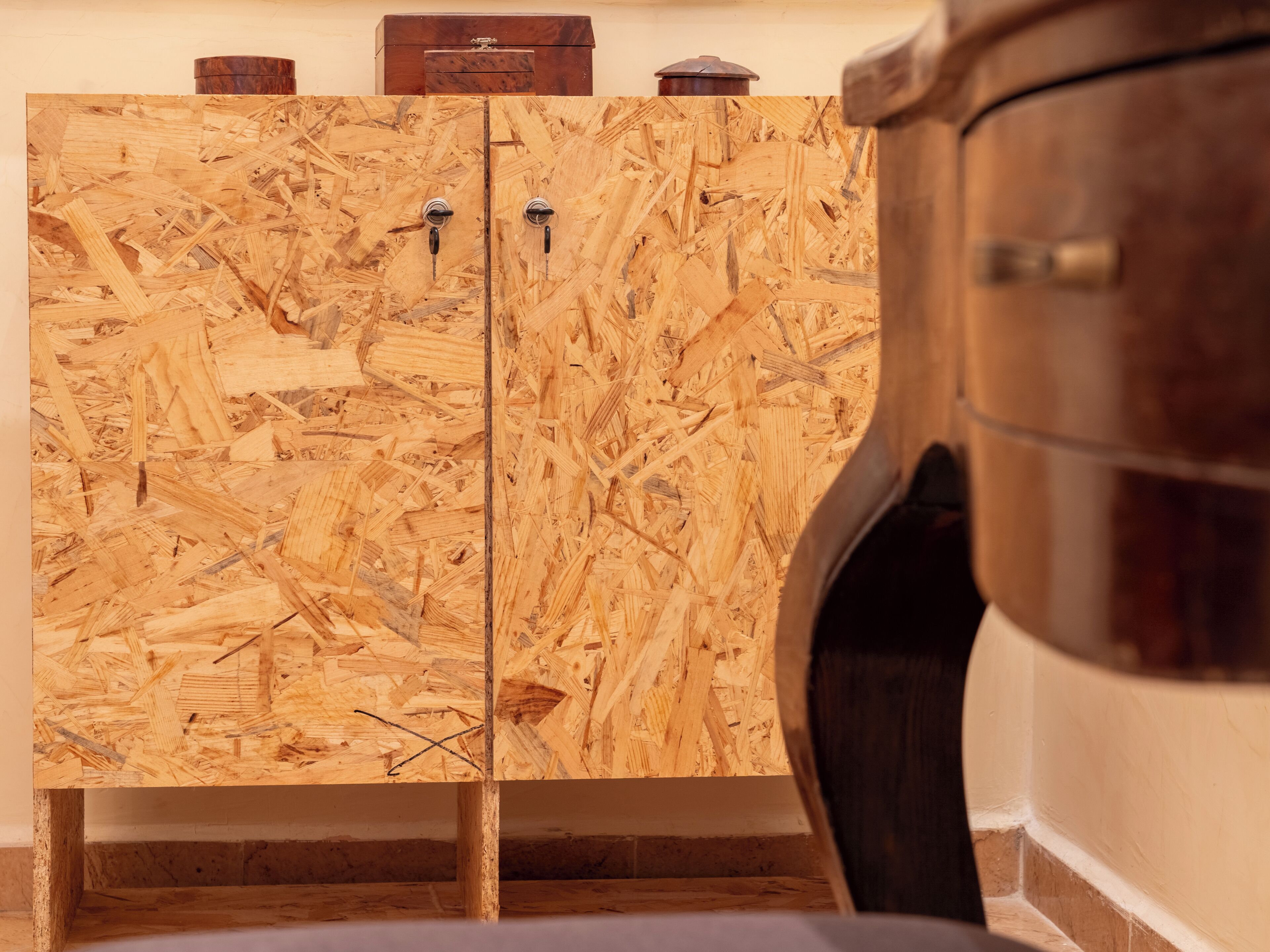 Ein Holzkabinent mit zwei Türen, eine kleine Holzkiste obenauf und ein zylindrisches Objekt auf der rechten Seite.