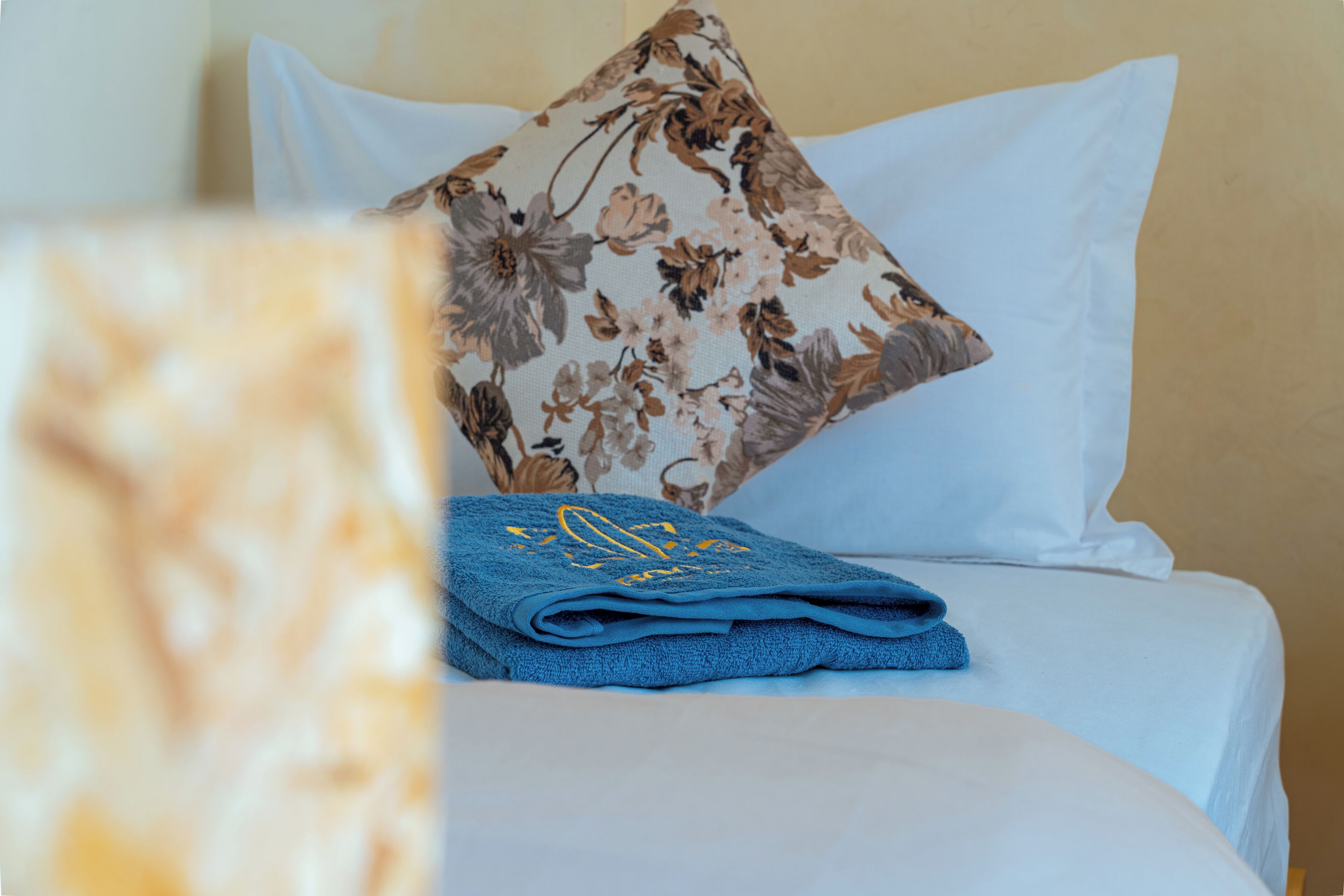 Ein ordentlich bezogenes Bett mit einem blauen Handtuch, weißen Kissen und einem Kissen mit Blumenmuster.