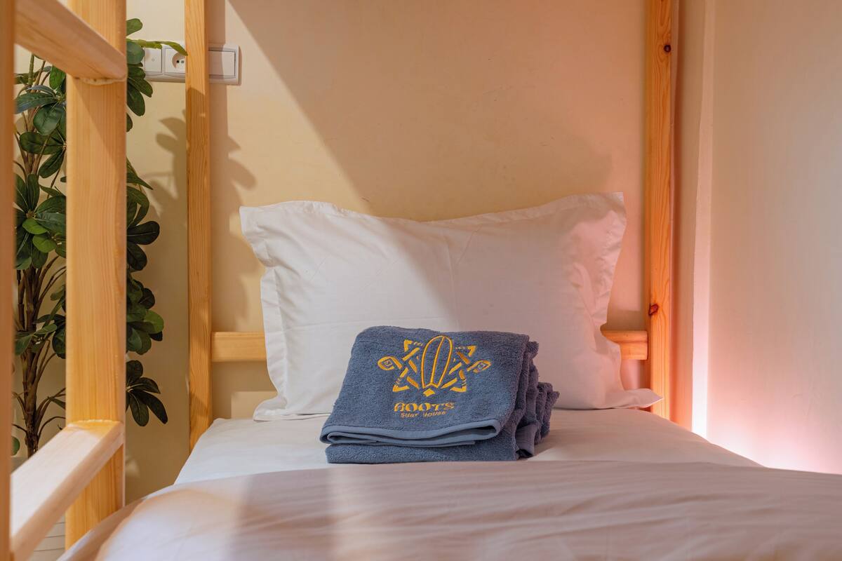 A single bed with a white pillow and a folded towel with a logo.