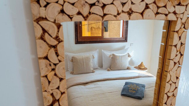 Un dormitorio con cama, almohadas, mesita de noche y espejo con marco de madera.