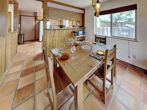 A dining area with a wooden table set for two, a kitchen in the background, and a window with a view of trees. - Casa Carmilita | Southwestern Charmer + Spacious Backyard (Santa Fe)