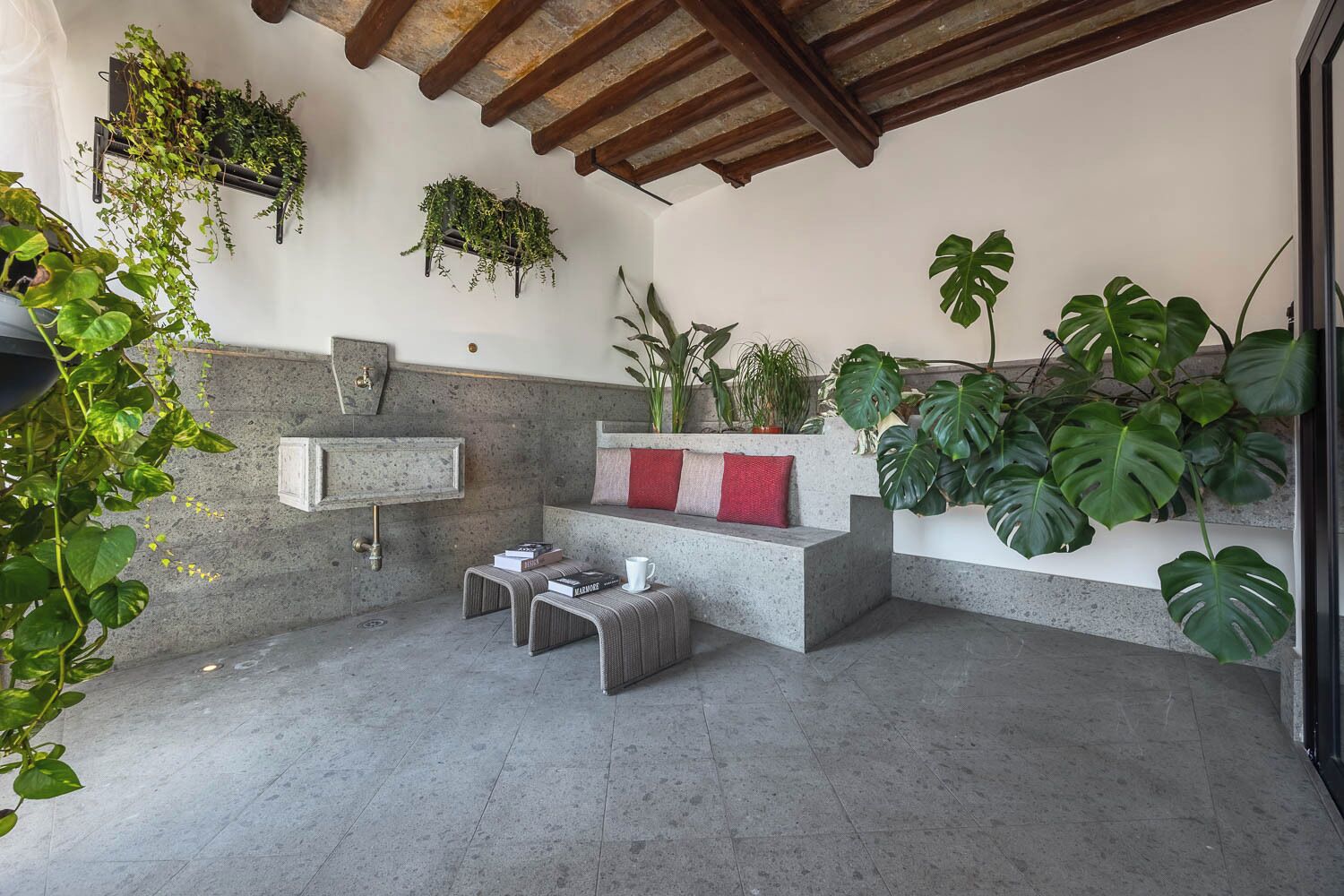 A modern outdoor seating area with a stone bench, a small table, and various potted plants.