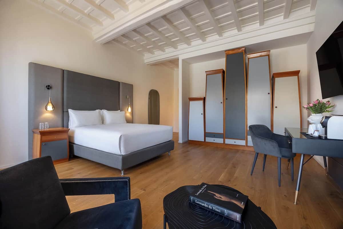 Ein modernes Hotelzimmer mit einem Bett, Nachttischen, einem Schreibtisch, einem Sessel und einem Kleiderschrank.