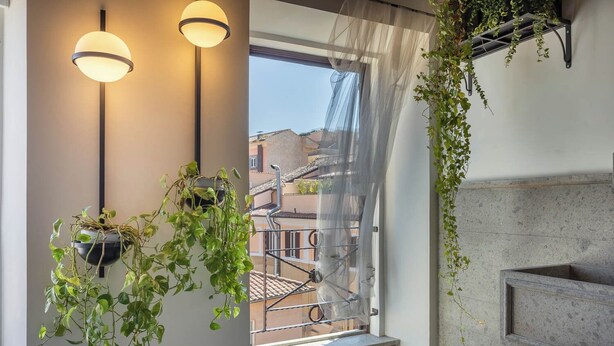 A balcony with hanging plants, a window with a view of buildings, and a wall-mounted shelf. - Ara di Marte Living Art (Rome)