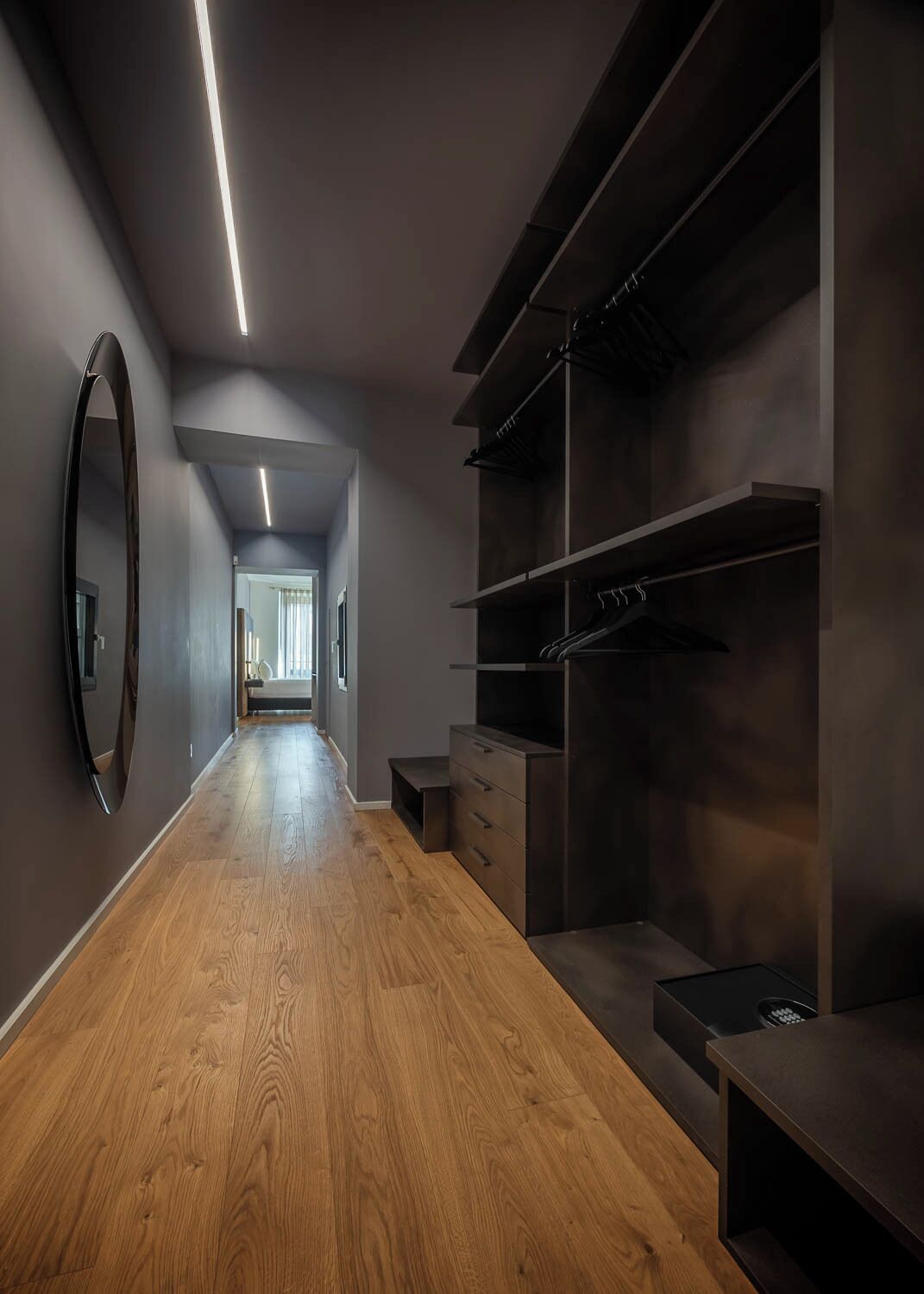 Un pasillo moderno con suelo de madera, un espejo grande y un vestidor con estantes y cajones.