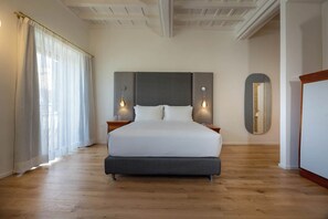 Una cama grande con un cabecero oscuro, dos mesitas de noche con lámparas, un espejo grande y un piso de madera.