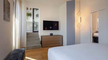 Un dormitorio con cama, cómoda, televisor y una escalera que lleva a un balcón.