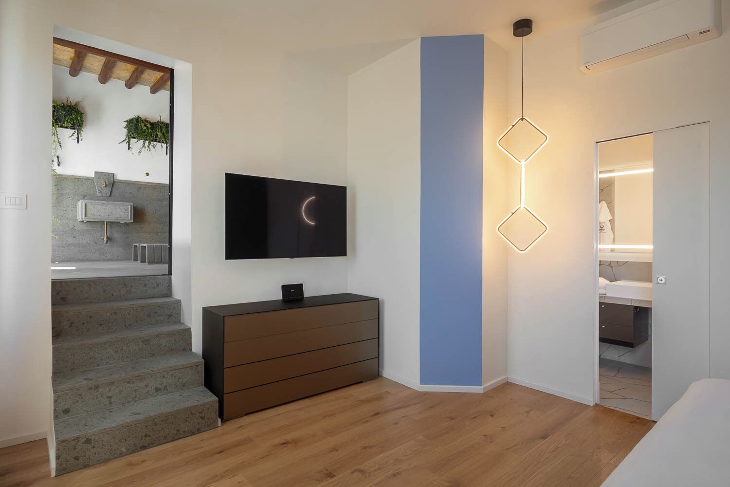 A modern interior with a staircase, a flat-screen TV, a wall-mounted light fixture, and a bathroom visible through an open door.