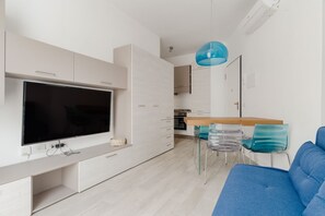 Eine moderne Küche mit Flachbildfernseher, weißen Schränken, einer Essecke mit Holztisch und -stühlen sowie einem blauen Sofa.