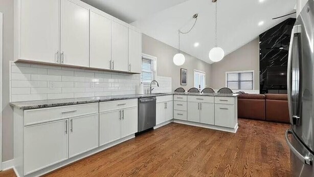 Una cocina moderna con armarios blancos, un refrigerador de acero inoxidable y piso de madera.