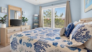 Een slaapkamer met een bed, een dressoir, een televisie, een plafondventilator en een raam met gordijnen.