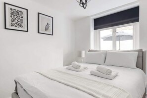 Quarto de hotel com uma cama, duas obras de arte emolduradas, uma janela com vista e um abajur.