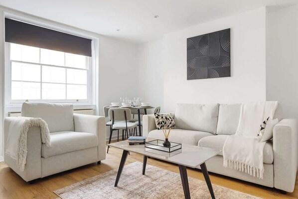 Uma sala de estar moderna com sofá, poltrona, mesa de centro e um espaço de jantar com cadeiras e mesa.