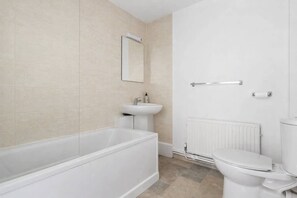 Uma casa de banho moderna com banheira, lavatório, sanita e espelho.