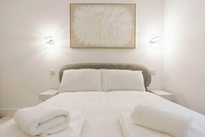 Ein Hotelzimmer mit einem Bett, weißen Laken, einem Kopfteil, zwei Nachttischen und einem Wandbild.
