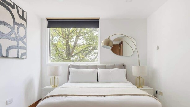 Quarto moderno com uma cama grande, duas mesas de cabeceira, uma janela com vista para árvores e um espelho fixado na parede.