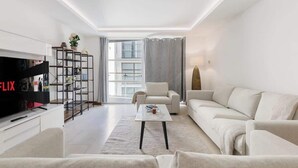 Uma sala de estar moderna com televisão de tela plana, um sofá, uma mesa de centro, uma estante e uma janela grande.