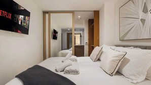 A hotel room with a bed, a flat-screen TV, a mirror, and a door leading to another room. - Elegant Fitzrovia Flat in Central London (London)