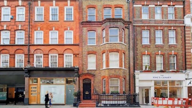 A row of red brick townhouses with uniform window designs, a black storefront with a green door, and a sign for 'The King's Canary' hotel. - Elegant Fitzrovia Flat in Central London (London)