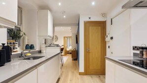A modern kitchen with white cabinetry, a wooden door, and a central island with a sink and stove. - Elegant Fitzrovia Flat in Central London (London)
