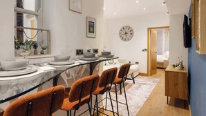 A modern dining area with a glass table, orange chairs, and a clock on the wall. - Elegant Fitzrovia Flat in Central London (London)