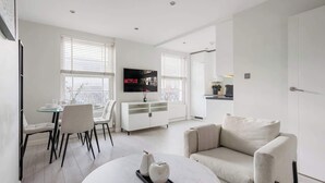 Una sala de estar moderna con un sofá blanco, un comedor con una mesa de vidrio y un televisor montado en la pared.