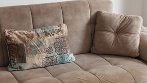 Ein braunes Sofa mit einem gemusterten Kissen und einem Glastisch mit Kerze und Fernbedienung.