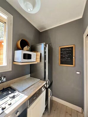 Une cuisine compacte équipée d’un four à micro-ondes, d’une cuisinière et d’un réfrigérateur. Un tableau noir sur lequel sont écrits des messages motivants est accroché au mur.