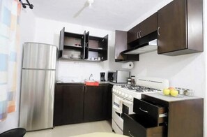 A compact kitchen with a refrigerator, stove, microwave, and dark wooden cabinets.