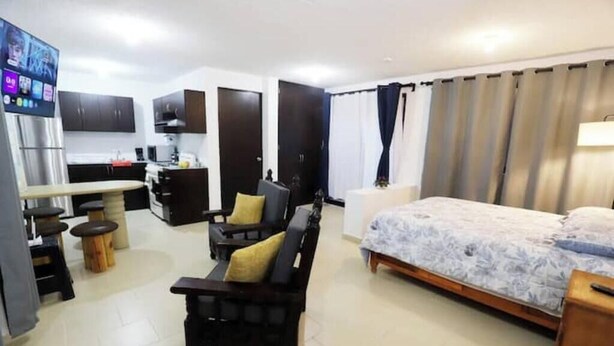 A compact room with a bed, a sofa, a small kitchen area, and a TV. - Spacious and quiet apartment PKG free of charge (San Miguel de Allende)