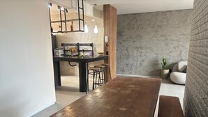 A modern kitchen with a wooden table and bar stools, a hanging light fixture, and a stone wall. - Apartment on Praia do Futuro beach, 200m from the sea. (Fortaleza)