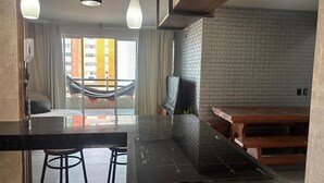 A modern kitchen with a black countertop, two stools, a hanging light fixture, and a brick wall. - Apartment on Praia do Futuro beach, 200m from the sea. (Fortaleza)