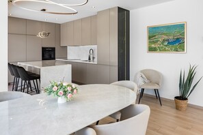 Eine moderne Küche mit einer Marmorinsel, Barhocker, einem Esstisch mit Blumenvase und einem großen Gemälde an der Wand.