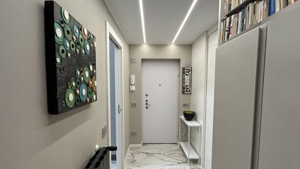A hallway with a marble floor, a radiator, a door, and a bookshelf with books. - Cerano8 Design Apartment Tortona District (Milano)