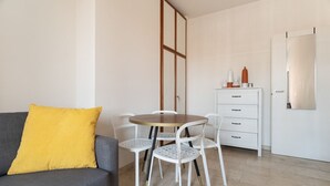 Een moderne woonkamer met een grijze bank, een ronde houten tafel, witte stoelen, een witte dressoir en een grote spiegel aan de muur.