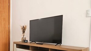 A flat-screen TV on a wooden TV stand with a white cabinet below. - Comfortable 2-Bedroom AC Apartment  Prime Location for Corporate Travel (São José do Rio Preto)