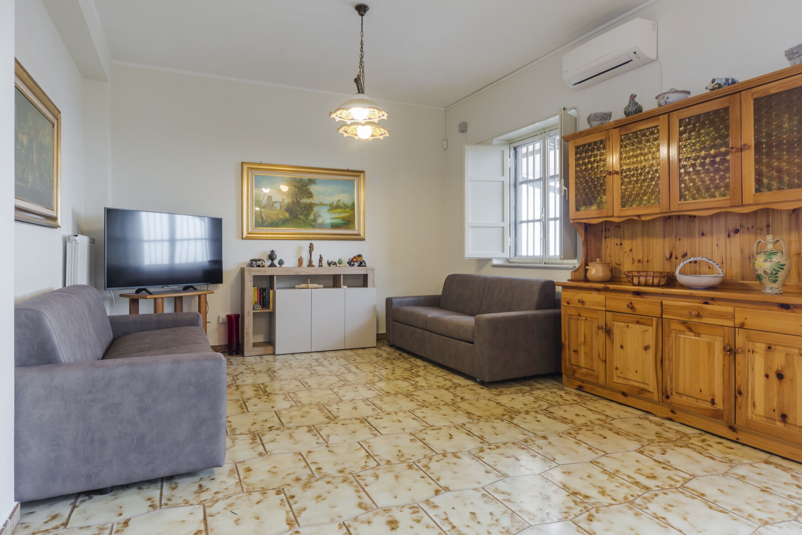 A living room with a sofa, a television, a cabinet, and a painting on the wall.