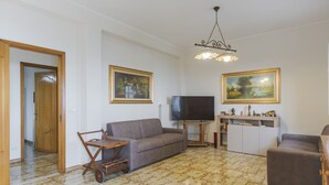 En stue med sofa, fjernsyn, skab i træ og to billeder på væggen.