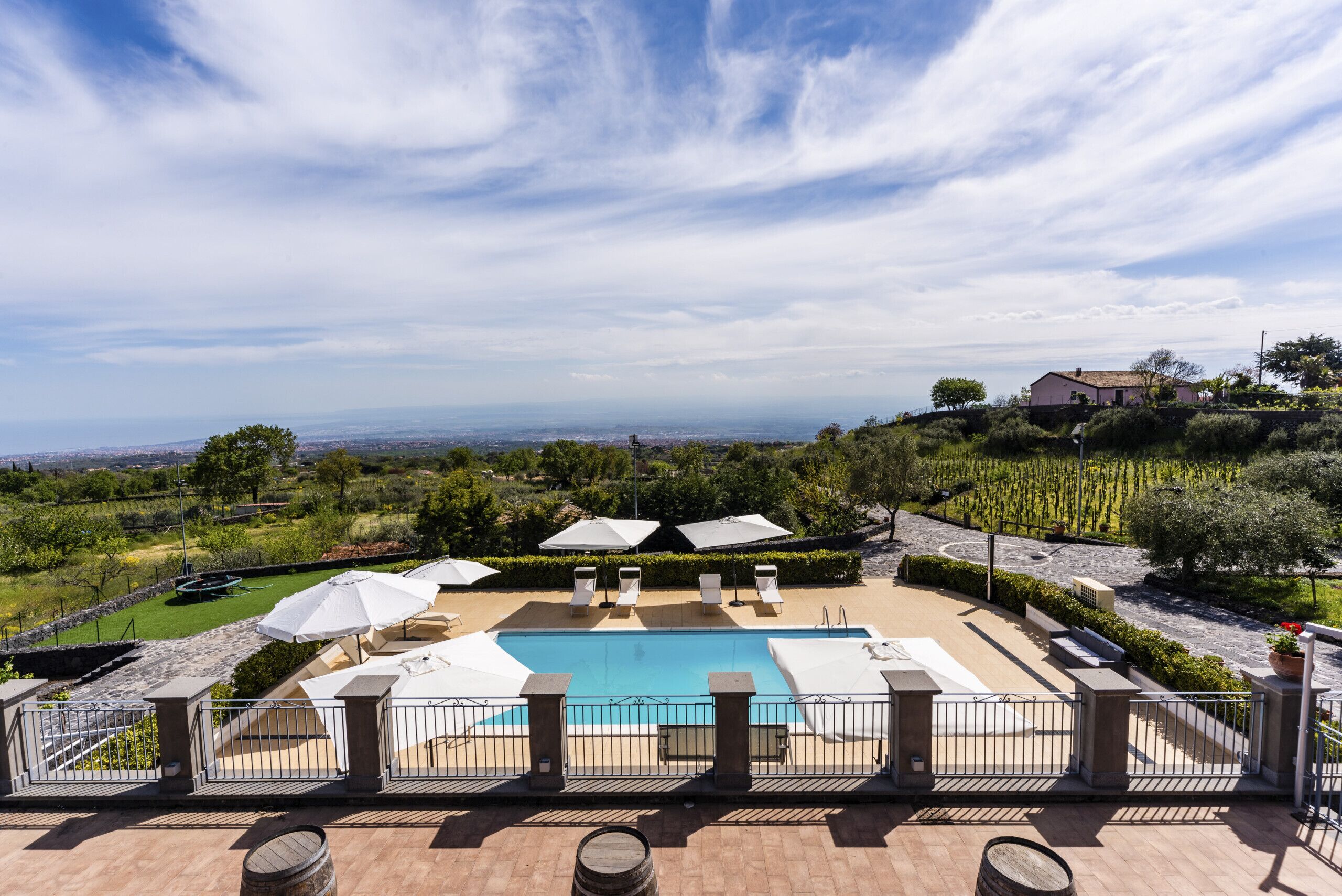 Piscina com espreguiçadeiras e guarda-sóis, cercada por uma grade, com vista para a paisagem.