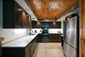 A kitchen with wooden ceiling, stainless steel appliances, and dark wooden cabinets. - Lake Namakagon Getaway for Boating, Fishing & Trail Riding (Cable)