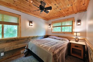 A bedroom with a wooden ceiling, two windows with blinds, a bed with a blanket, a nightstand with a lamp, and a ceiling fan. - Lake Namakagon Getaway for Boating, Fishing & Trail Riding (Cable)