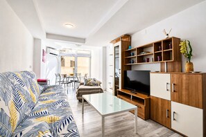 Een moderne woonkamer met een bank, televisie, houten kasten en een glazen salontafel.
