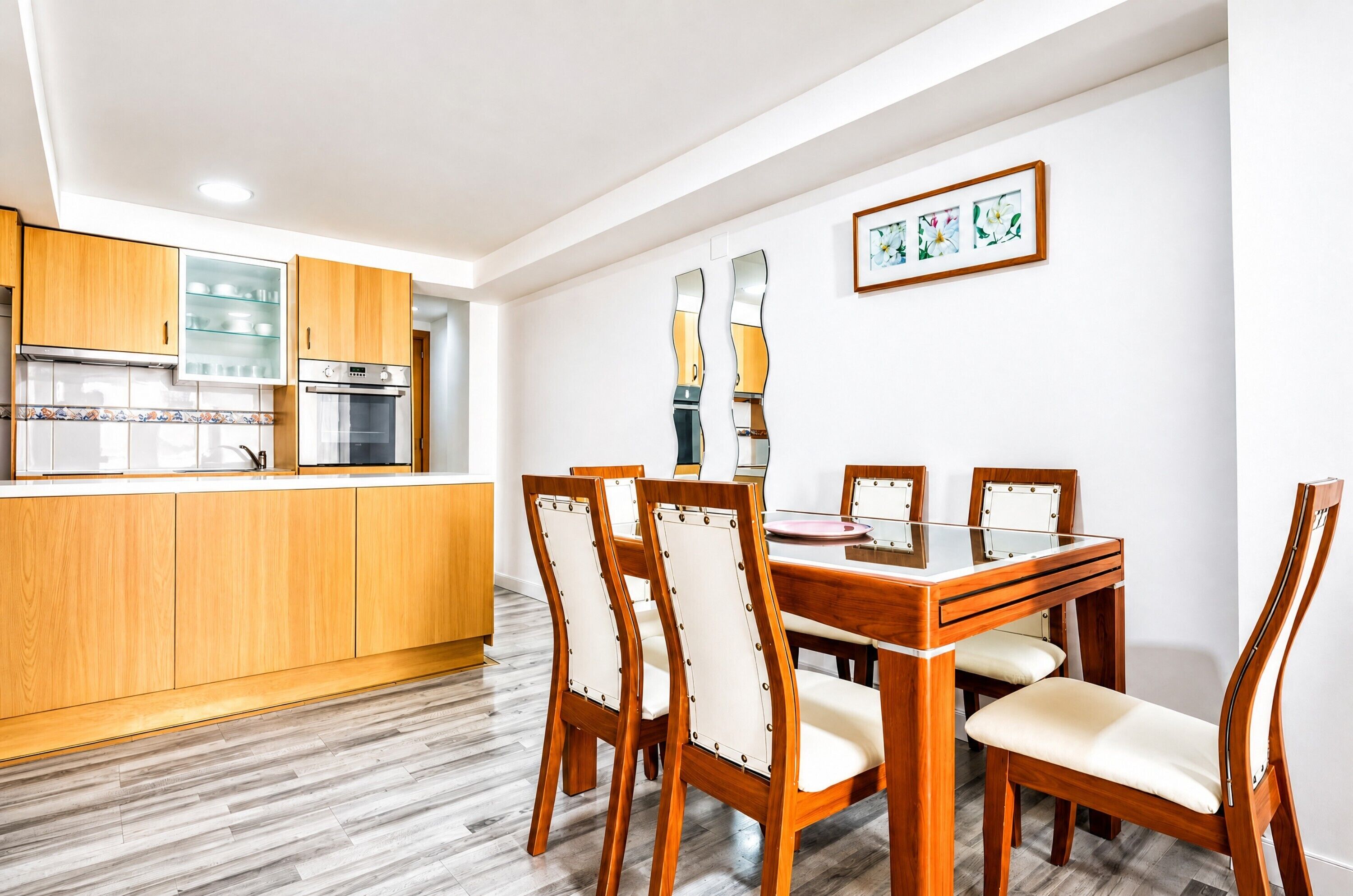 Une cuisine moderne avec des meubles en bois, un four encastré et un coin repas comprenant une table et des chaises en bois.