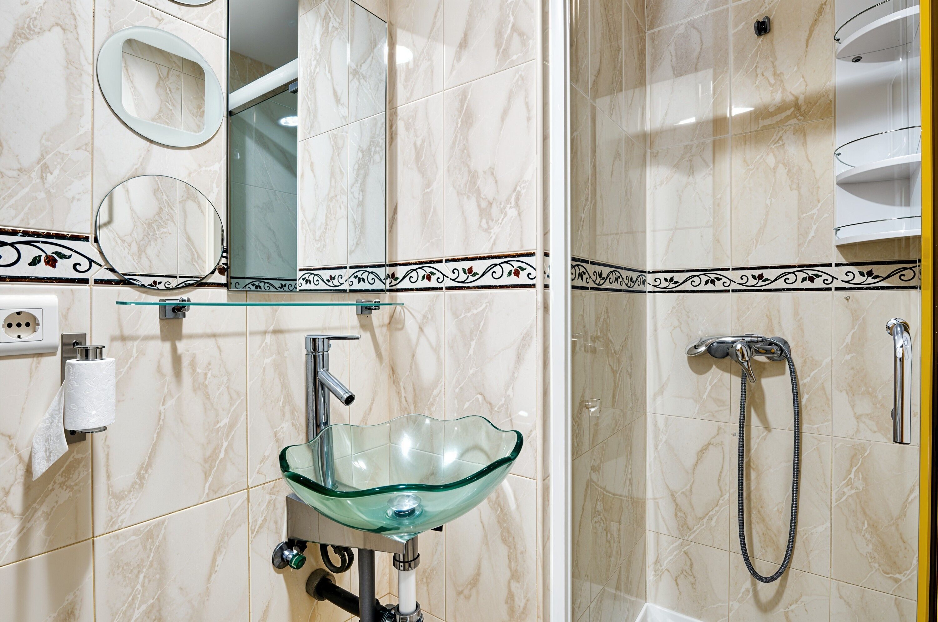 A bathroom with a glass bowl sink, a handheld showerhead, and a mirror with a decorative border.