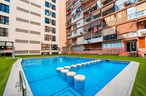 Ein Schwimmbecken im modernen Stil, umgeben von einer gepflegten Rasenfläche und angrenzenden mehrstöckigen Wohngebäuden.