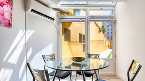 Ein moderner Essbereich mit einem Glastisch und Metallstühlen, einem großen Fenster mit Jalousien und Blick ins Freie.
