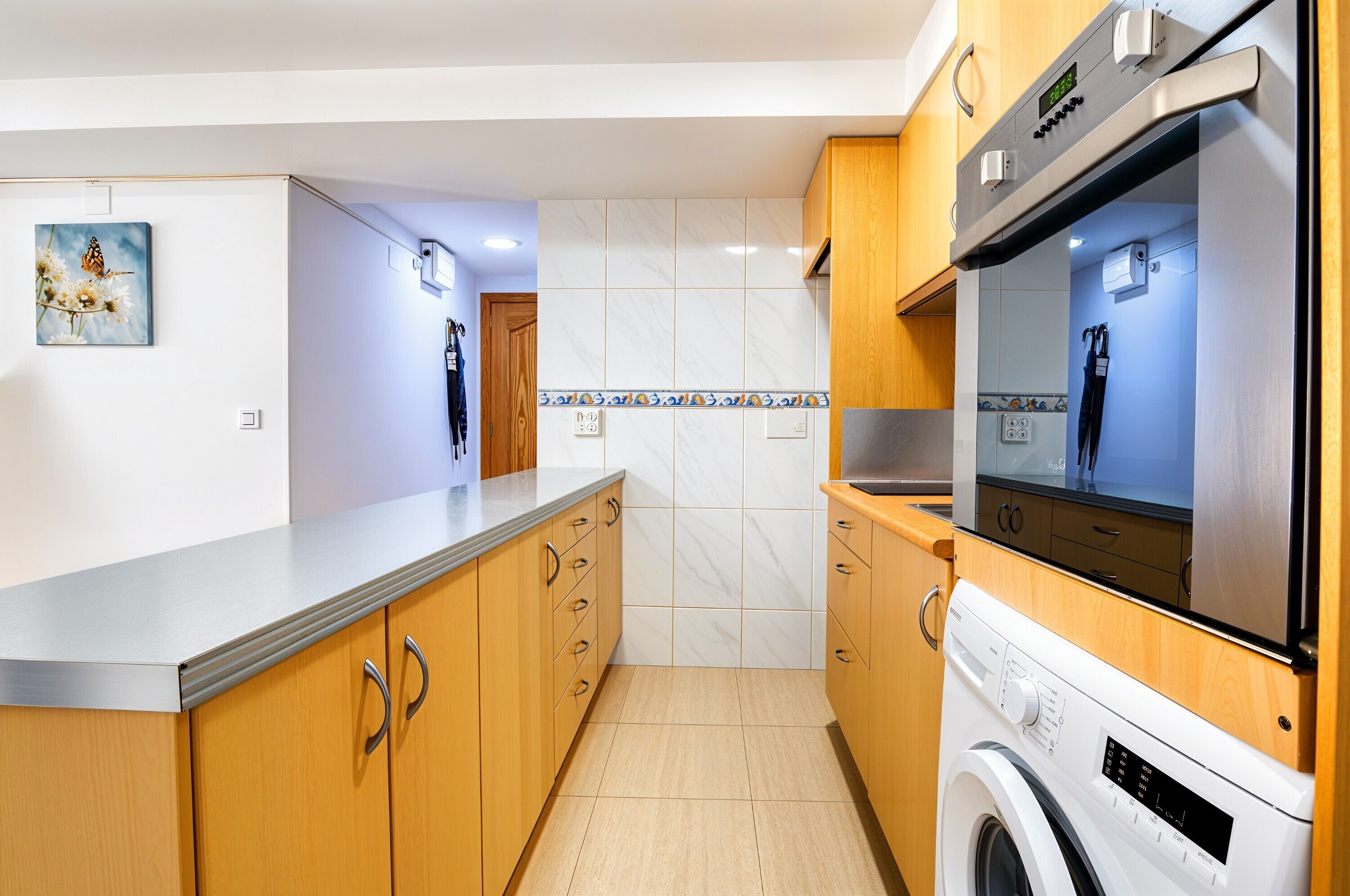 A modern kitchen with wooden cabinets, a built-in washing machine, and a tiled backsplash.