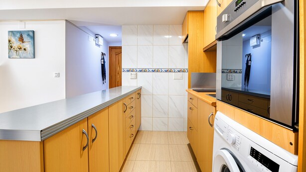 Eine moderne Küche mit Holzausbau, einer integrierten Waschmaschine und einer Fliesenwand.