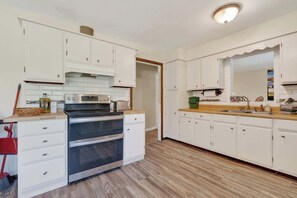 Una cocina con armarios blancos, horno empotrado, encimera de madera y un lavamanos.