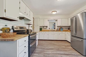 Una cocina moderna con armarios blancos, un refrigerador de acero inoxidable y una encimera de madera.